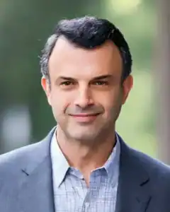 Man in a business suit smiling outdoors, professional headshot.